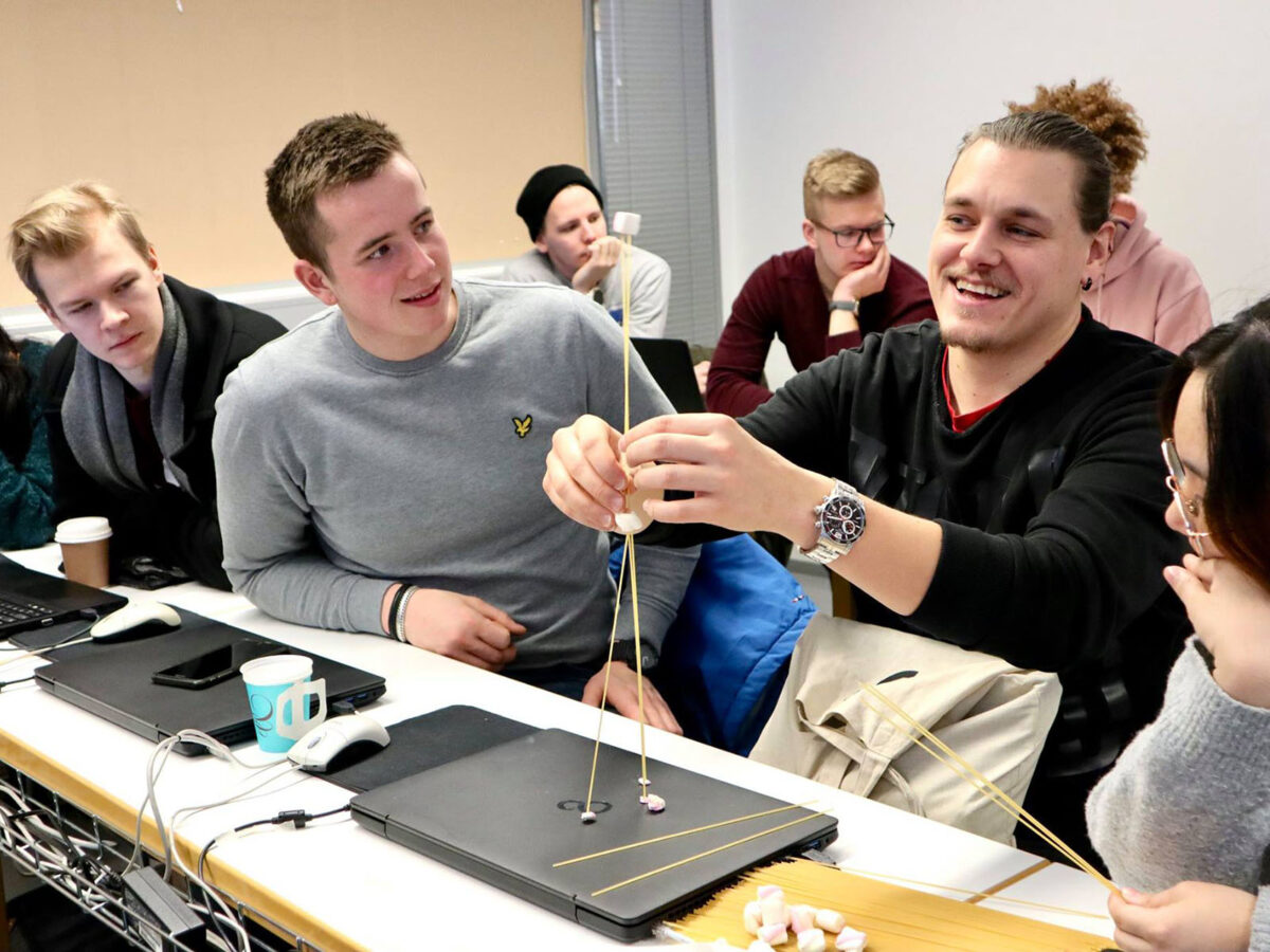 Business students building a construction with spaghetti and marshmallows. They are looking and the construction and smiling.