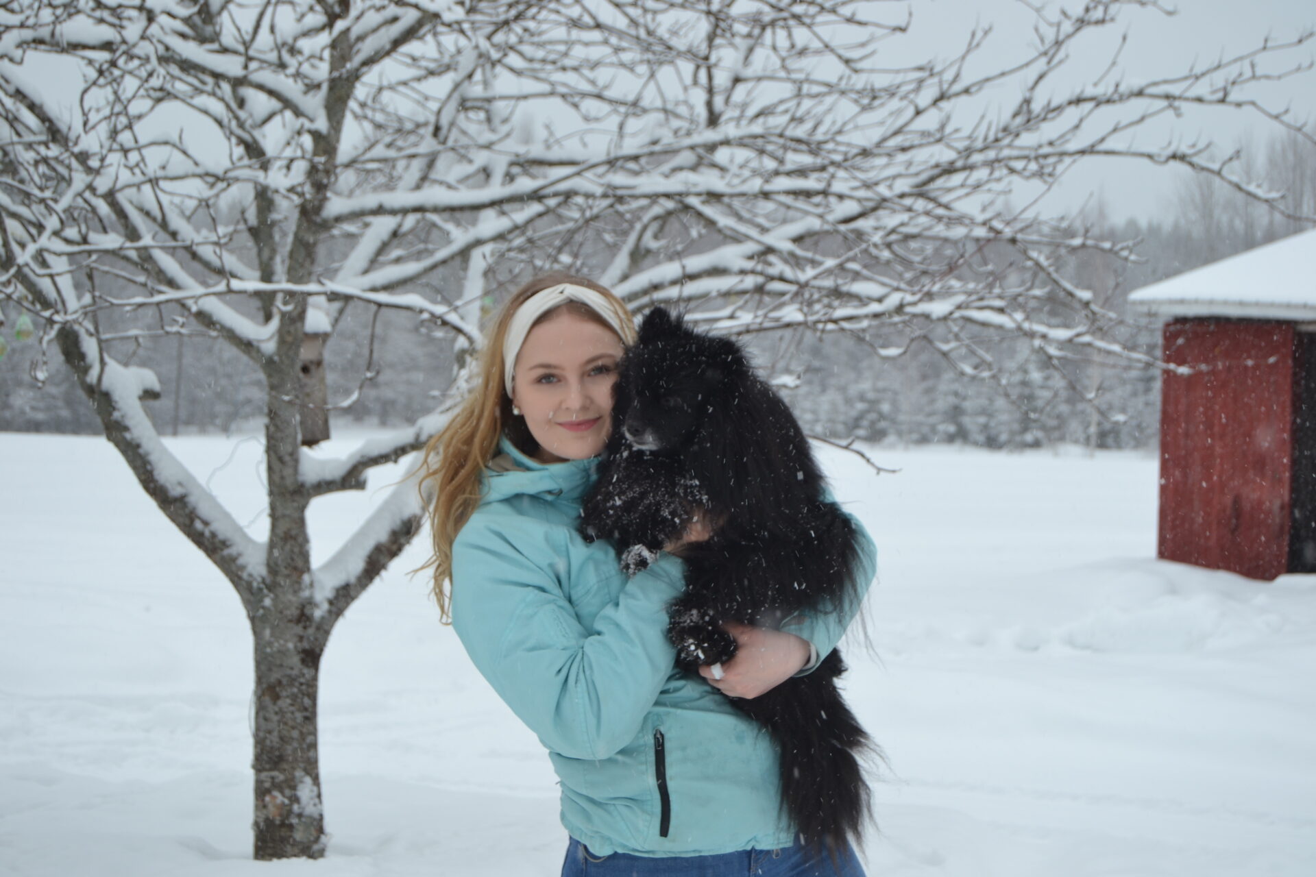 Nuori nainen koira sylissä talvimaisemassa.