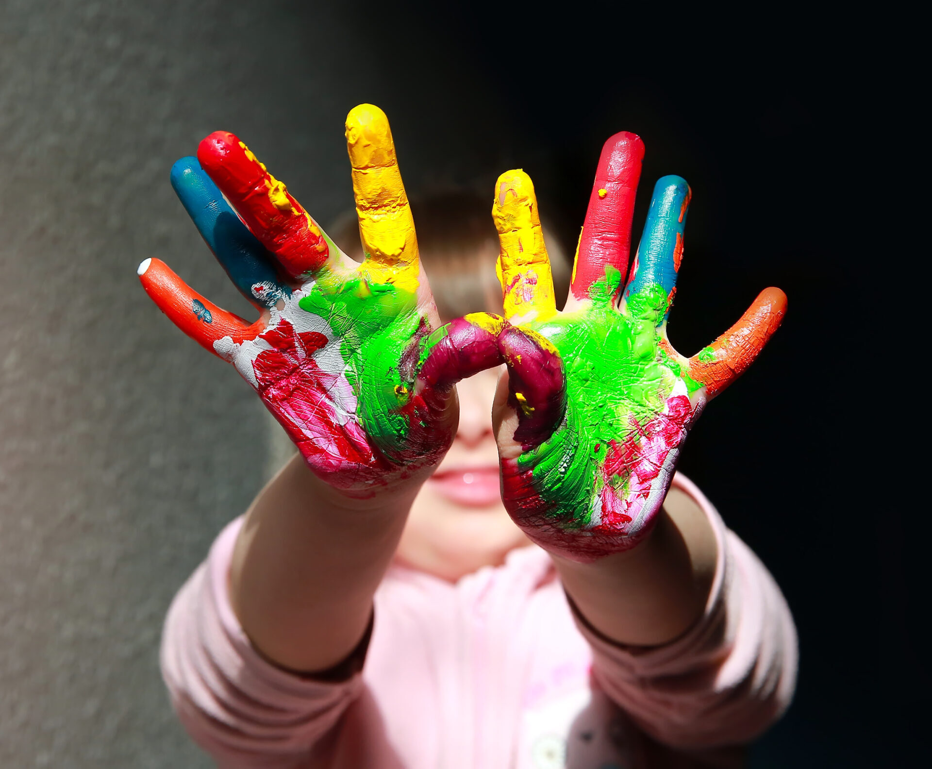 Tyttö kädet ojennettuna, sormet eri värisin öljyvärein maalattuina.