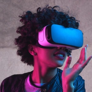 Kuvituskuva. Naine seisoo VR-lasit päässään ja katsoo kuvan oikealle puolelle kädet ilmassa.