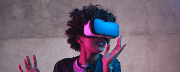 Kuvituskuva. Naine seisoo VR-lasit päässään ja katsoo kuvan oikealle puolelle kädet ilmassa.