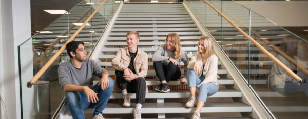 Opiskelijat istuvat kirjaston portailla. Kaikki hymyilevät ja katsovat toinen toisiaan.