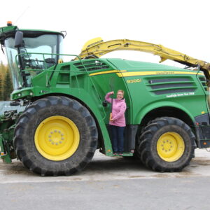 Iso vihreä traktori, jonka vieressä poseeraa hymyilevä nainen.