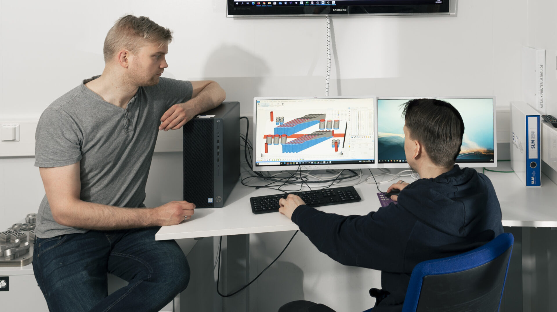 Kaksi miestä tietokoneella katsomassa teknisiä piirrustuksia