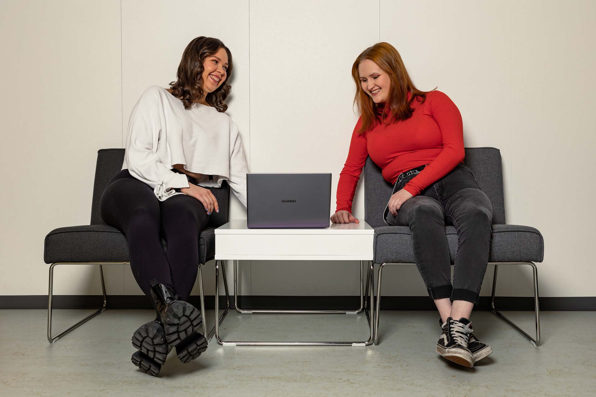 Kaksi naisopiskelijaa istuvat käytävän nojatuoleilla ja työskentelevät kannettavalla tietokoneella.
