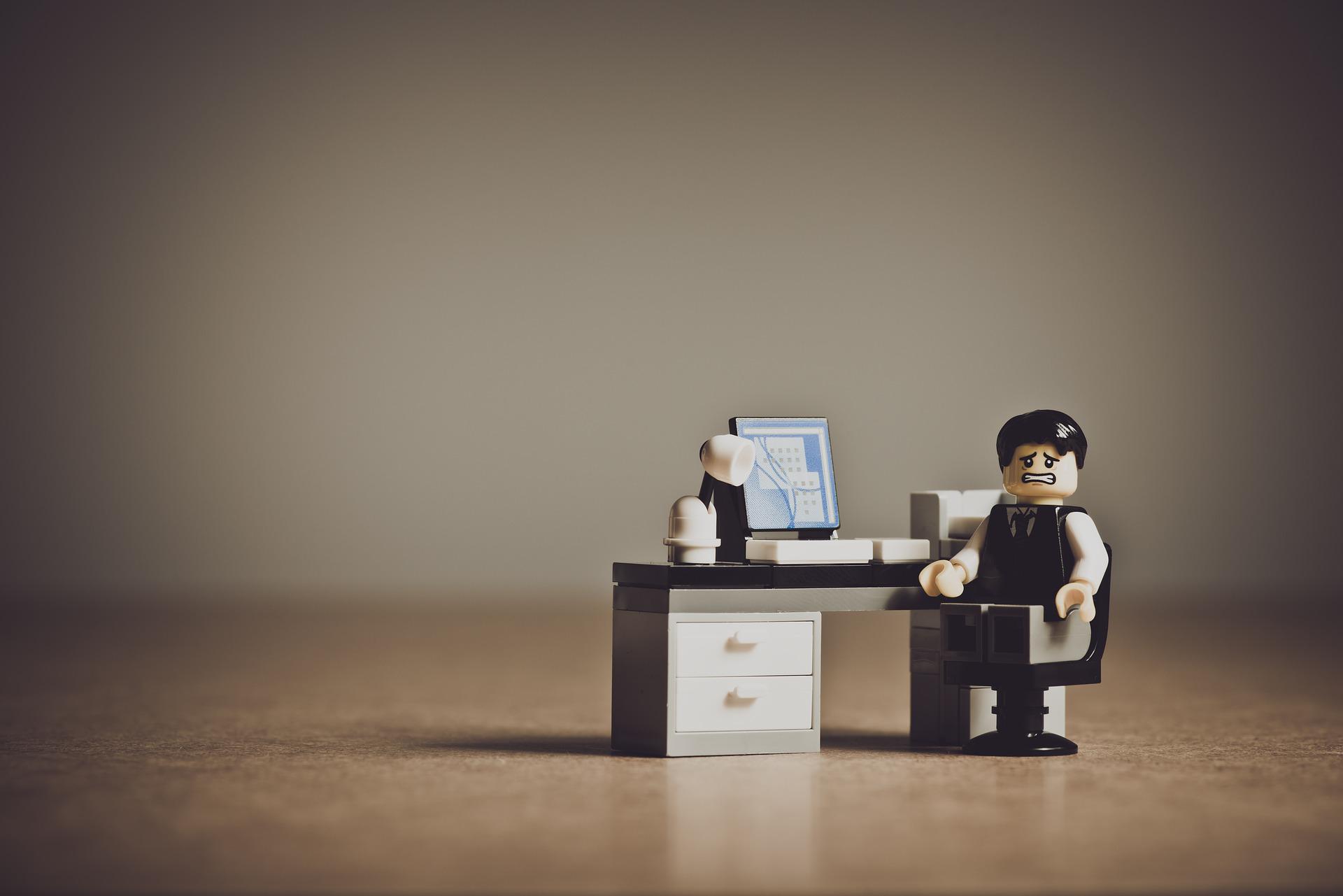 Lego-ukko istuu tietokoneen ääressä ja irvistää kameralle.