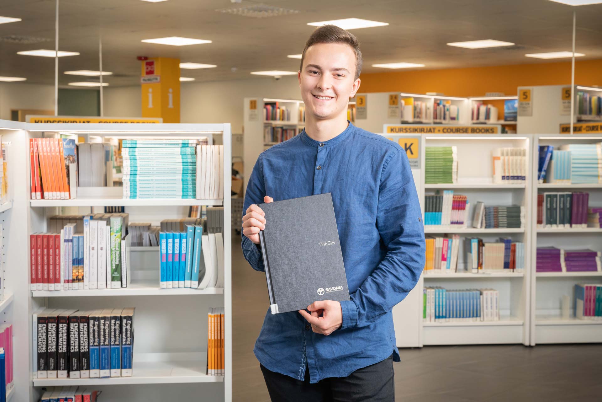 Opiskelija kirjastossa opinnäytetyö kädessään.