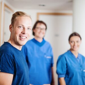 Kolme sairaanhoitajaa seisoo sinisissä asuissaan ja hymyilee kameralle.