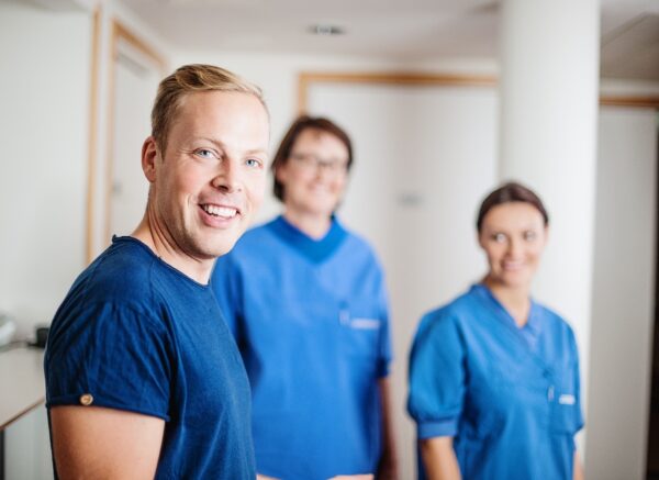 Kolme sairaanhoitajaa seisoo sinisissä asuissaan ja hymyilee kameralle.