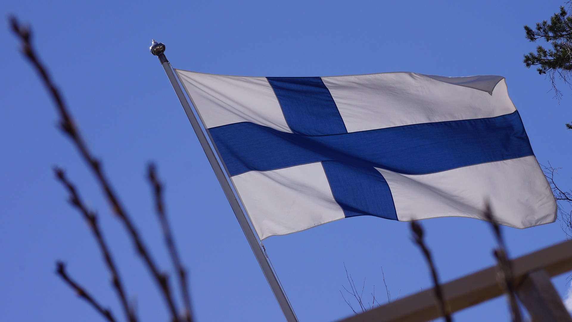 Suomen lippu lipputangossa sinistä taivasta vasten