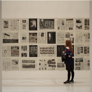 Nainen seisoo seinän edessä, jossa on esillä taidetta.