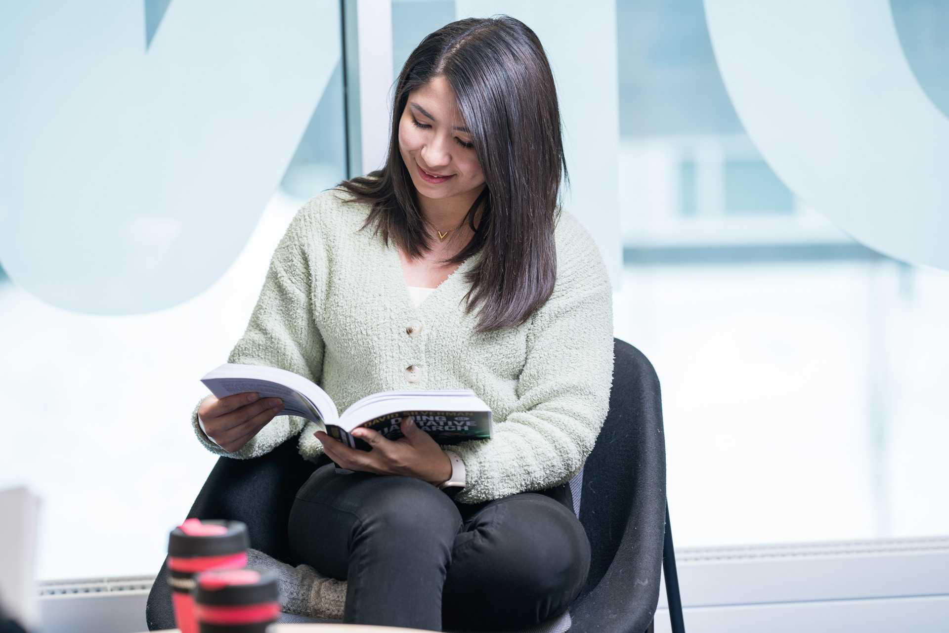 Opiskelija istuu kirjastossa kirja kädessä.