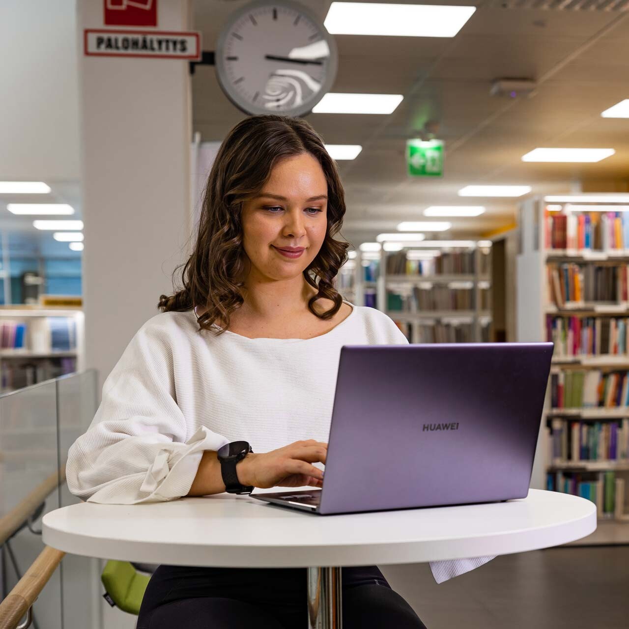 Opiskelija istuu kirjaston työpisteellä ja työskentelee kannettavalla tietokoneella.