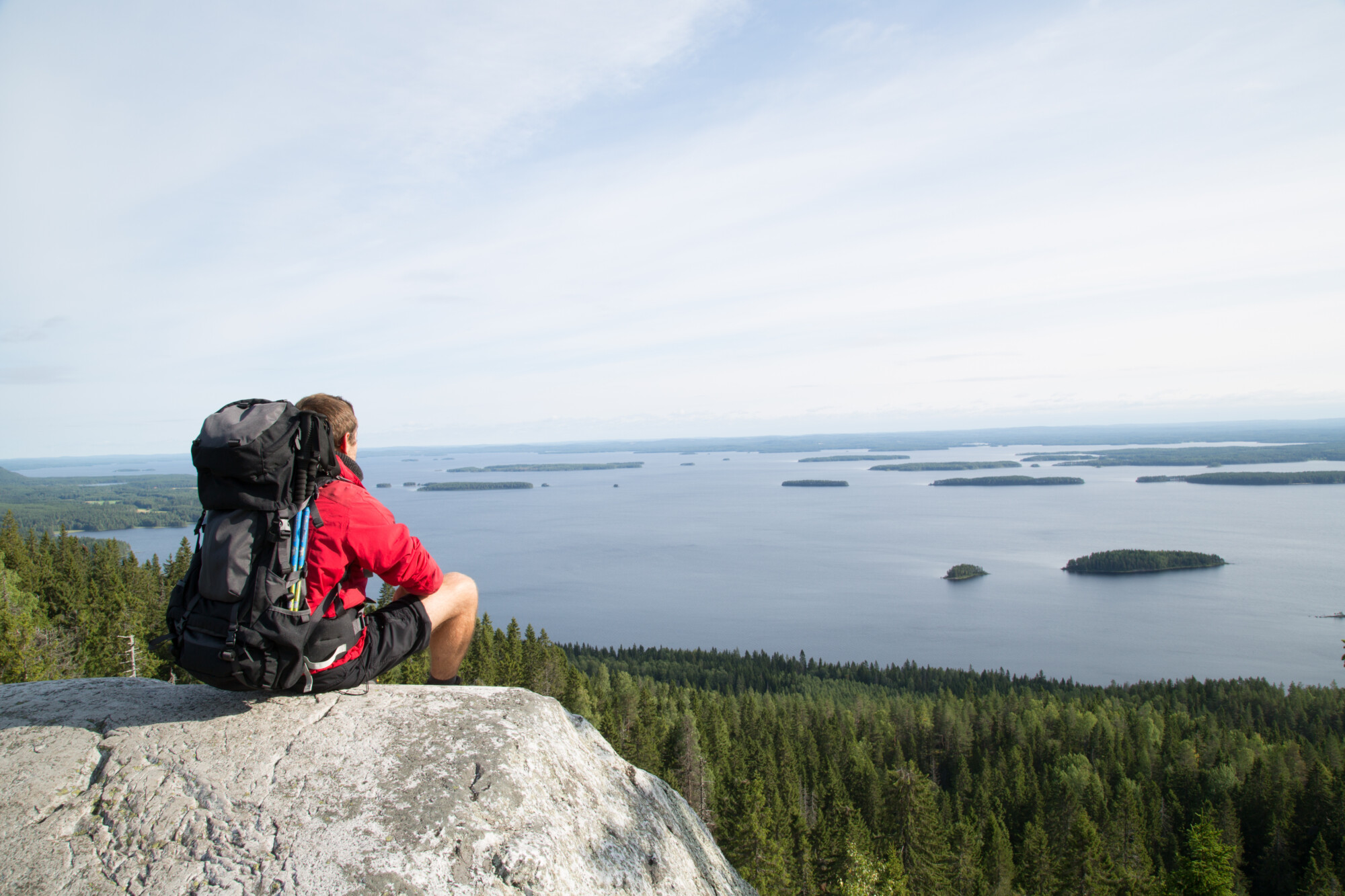Hiker sits on the summit Paha-Koli and enjoys the scenery of the Pielinen lake, summer