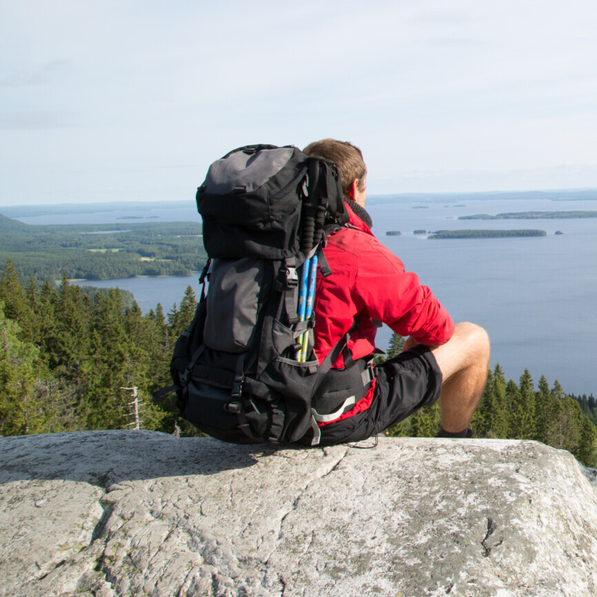 Hiker sits on the summit Paha-Koli and enjoys the scenery of the Pielinen lake, summer