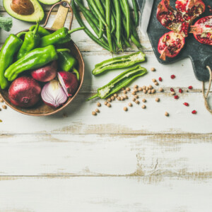 Winter vegetarian, vegan food cooking ingredients. Flat-lay of vegetables, fruit, beans, cereals, kitchen utencil, dried flowers, olive oil over white wooden background.