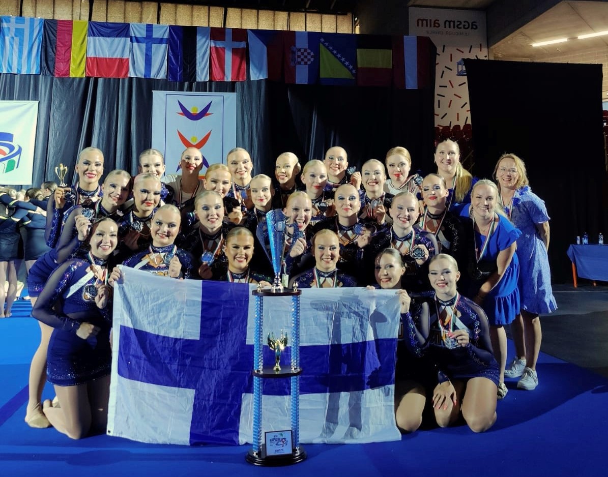 cheertanssijoukkue ryhmittyneenä Suomen lipun taakse