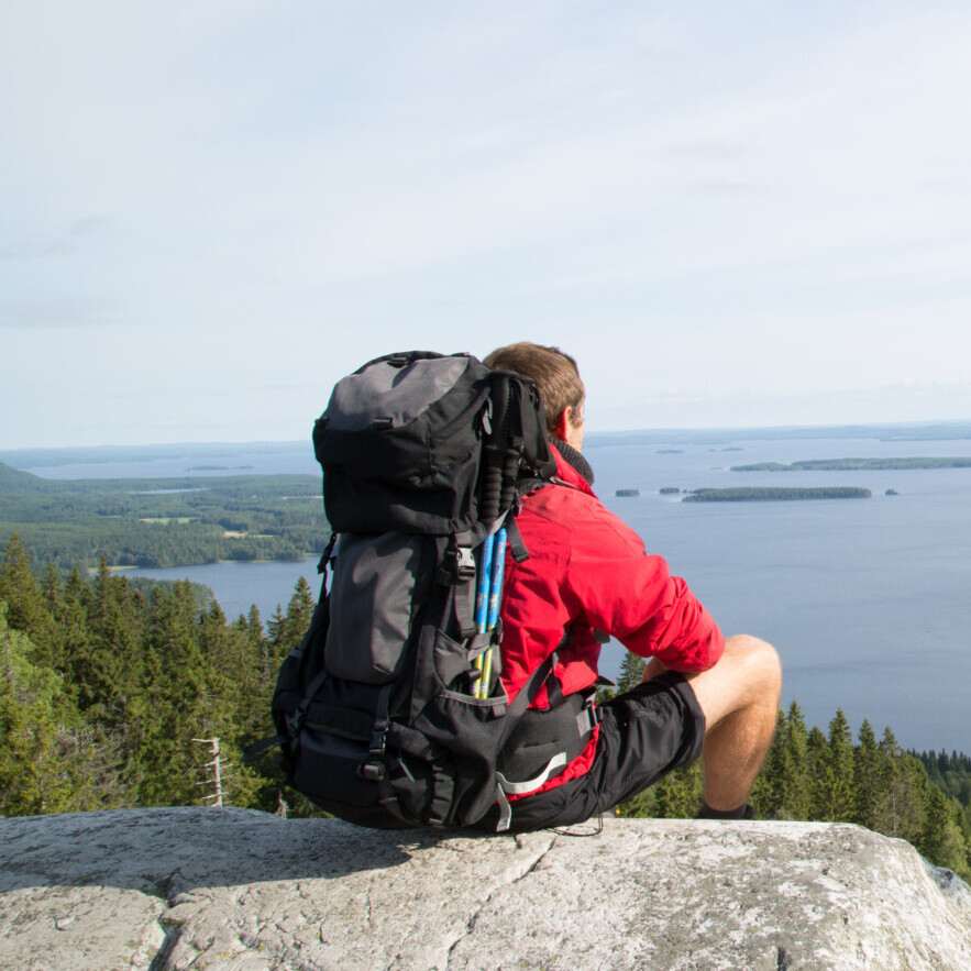 Hiker sits on the summit Paha-Koli and enjoys the scenery of the Pielinen lake, summer