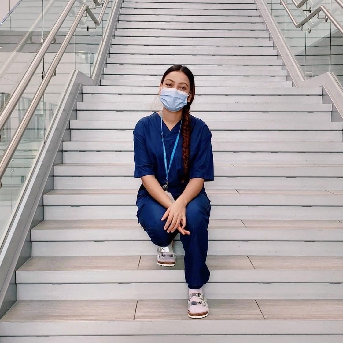 Sairaanhoitaja istuu portailla kasvoillaan maski.