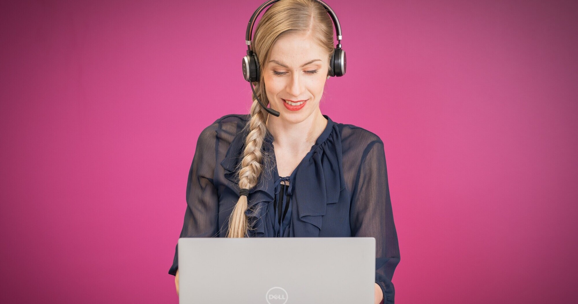 Nainen kuulokkeet ja mikrofoni päässä,kannettavan äärellä.