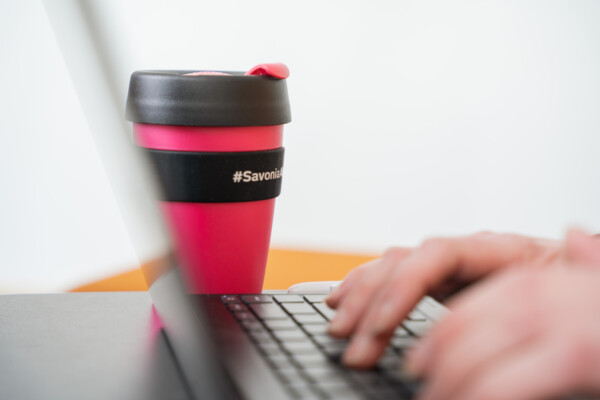 Sormet läppärin näppäimillä termosmuki vieressä