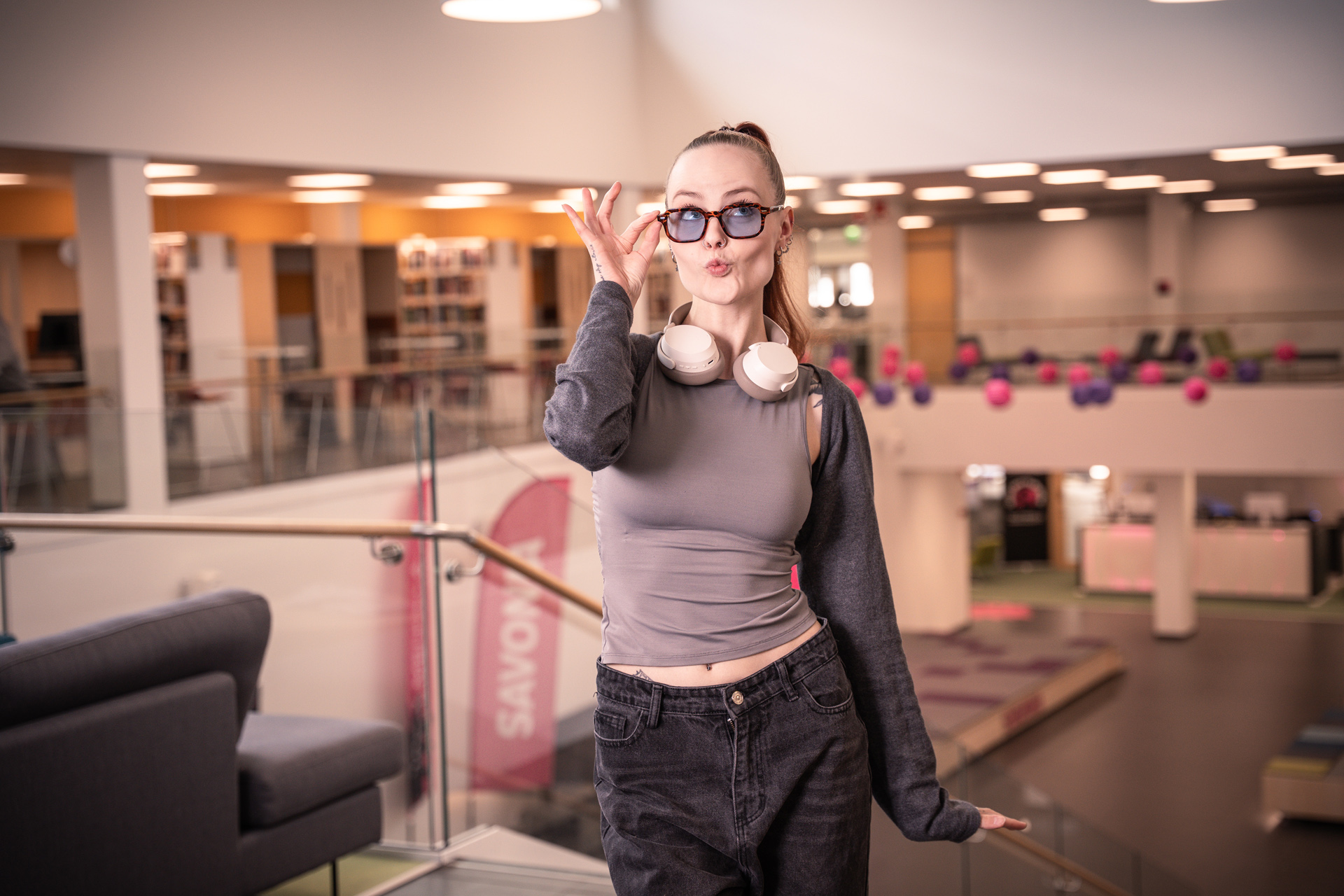 Naisopiskelija poseeraa ja hassuttelee kirjastossa.