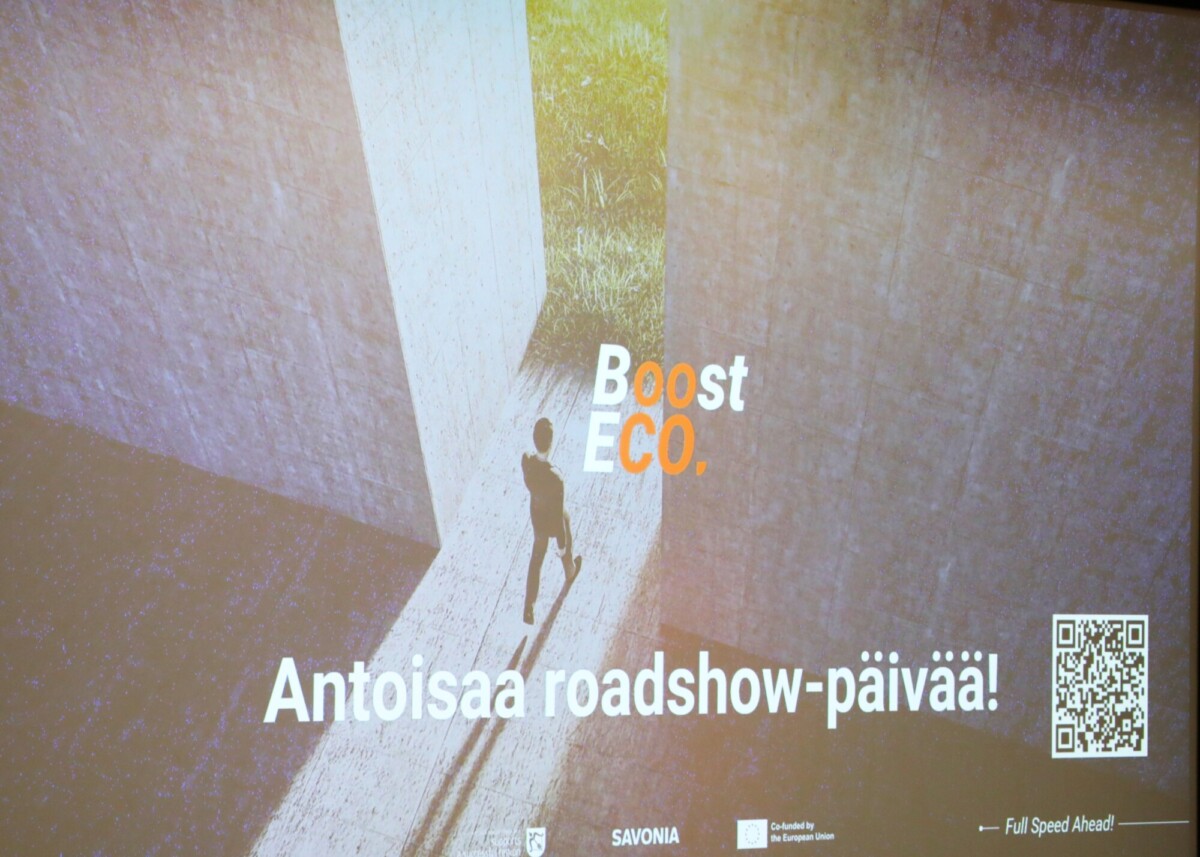 Henkilö kävelee kahden seinän välistä raosta kohti vehreyttä. Tekstissä lukee Boost ECO. ja Antoisaa roadshow-päivää!, ja alareunassa on QR-koodi ja logoja.