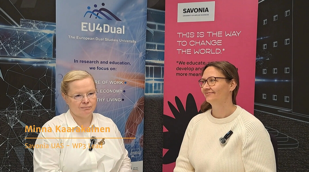 Kaksi naista istuu ja keskustelee EU4Dualin ja Savonian mainosten edessä. Toisella on silmälasit ja valkoinen villapaita; toisella on lyhyet vaaleat hiukset ja silmälasit. Näytöllä lukee: ”Minna Kaarakainen, Savonia UAS – WP3:n johtaja.”.