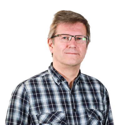 Keski-ikäinen mies, jolla on silmälasit ja lyhyet ruskeat hiukset, sinivalkoinen ruutupaita, seisoo valkoista taustaa vasten, katsoo kameraan ja hymyilee hieman.