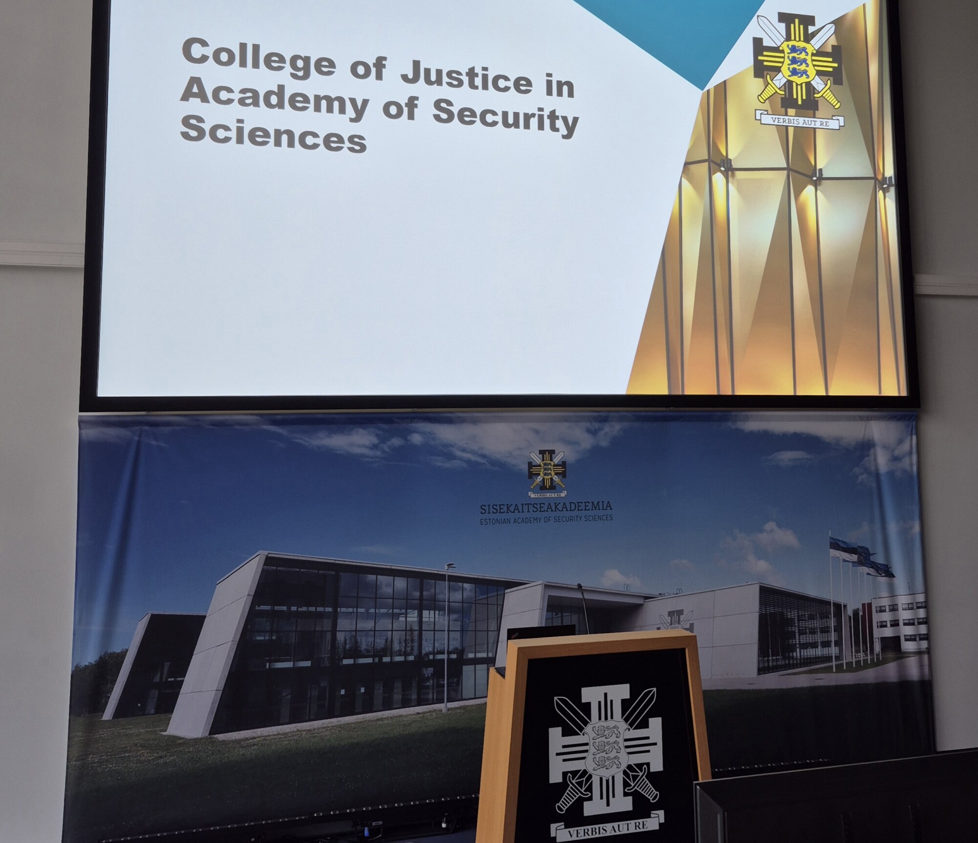 Esityksen diassa lukee College of Justice in Academy of Security Sciences. Alla on banderolli ja koroke, jossa on akatemian tunnus, ja taustalla näkyy moderni rakennus.