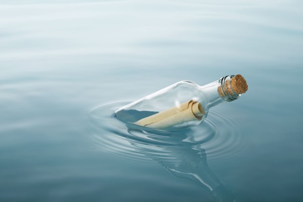 Lasipullo, jossa on korkki, kelluu tyynellä vedellä, ja sen sisällä on kääritty paperi tai viesti. Pulloa ympäröi kevyesti aaltoilu.