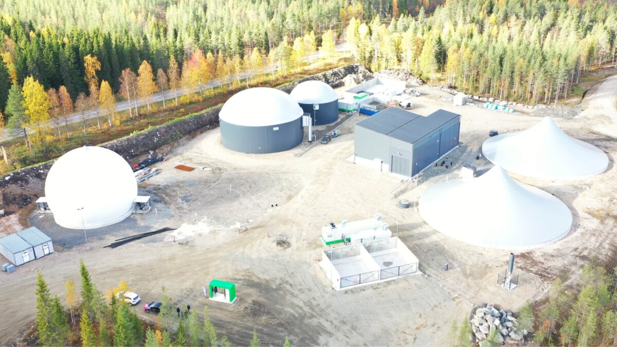 Ilmakuva metsän ympäröimästä biokaasulaitoksesta, jossa on useita suuria kupolimuotoisia varastosäiliöitä, kartiomaisia rakenteita ja suorakulmaisia rakennuksia raivatulla alueella.