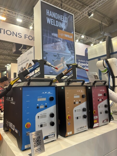 Kolme sinistä, pronssinväristä ja punaista käsikäyttöistä hitsauslaitetta on esillä messujen tiskillä, ja niiden yläpuolella on suuri kyltti, jossa lukee Handheld Welding LightWELD. QR-koodi on näkyvissä koneiden edessä.