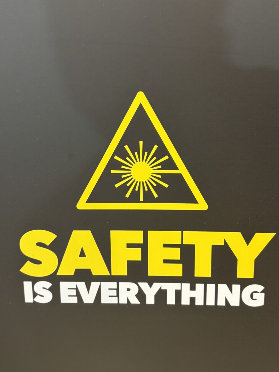 Keltainen varoituskolmio, jossa on säteilevä valosymboli lihavoidun tekstin SAFETY IS EVERYTHING yläpuolella tummalla pohjalla.