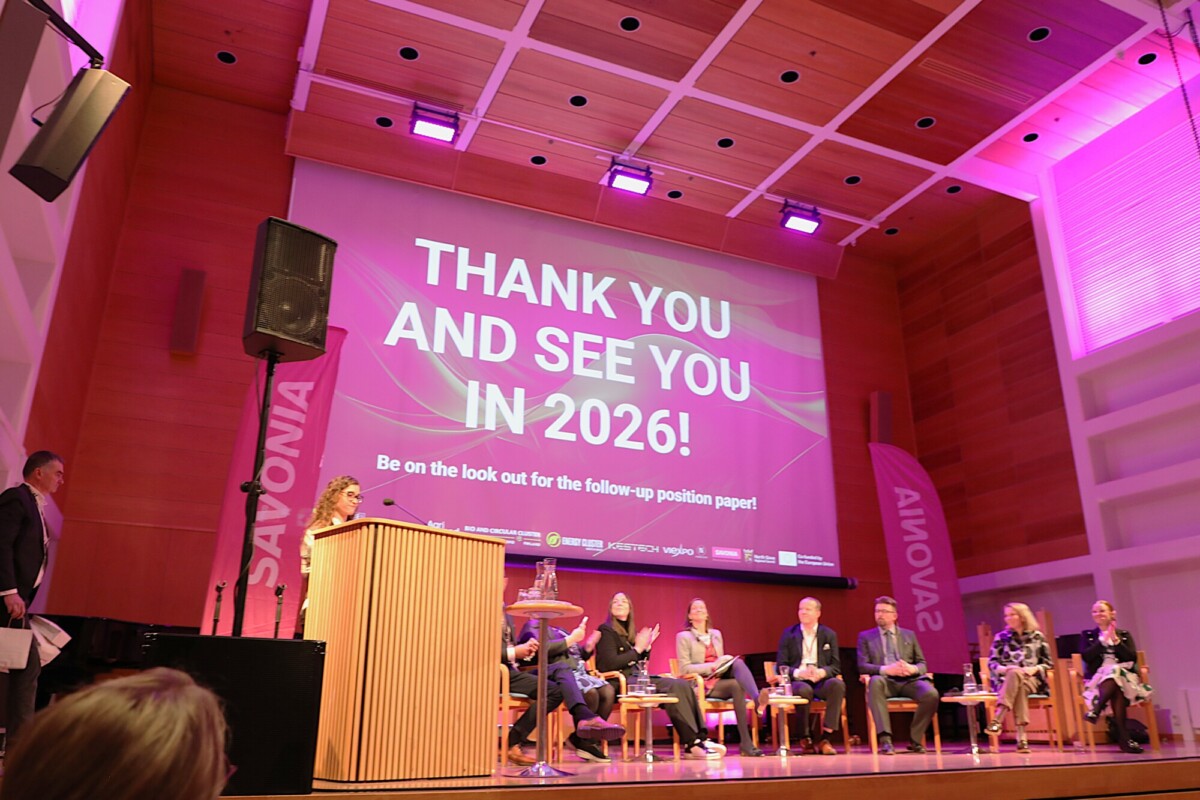 Lavalla istuu paneeli ihmisiä suuren näytön edessä, jossa lukee: Kiitos ja nähdään vuonna 2026! Pidä silmällä seurantaa koskevaa kannanottoa. Huone on valaistu vaaleanpunaisilla ja violeteilla valoilla.