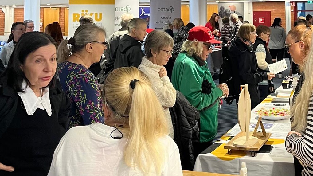 Vilkas sisätiloissa järjestetty tapahtuma, jossa ihmiset kokoontuivat pöytien ympärille esittelemään erilaisia tuotteita ja tiedotusmateriaalia. Osallistujat keskustelevat ja selaavat eri kojuja hyvin valaistussa huoneessa.