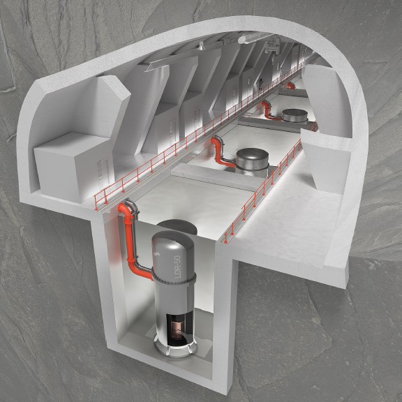 Maanalaisen laitoksen leikkausnäkymässä näkyy useita lieriönmuotoisia reaktoreita, jotka on yhdistetty oransseilla putkilla, ja niiden vieressä kulkee käytävä kallioon rakennetussa suuressa betonikammiossa.