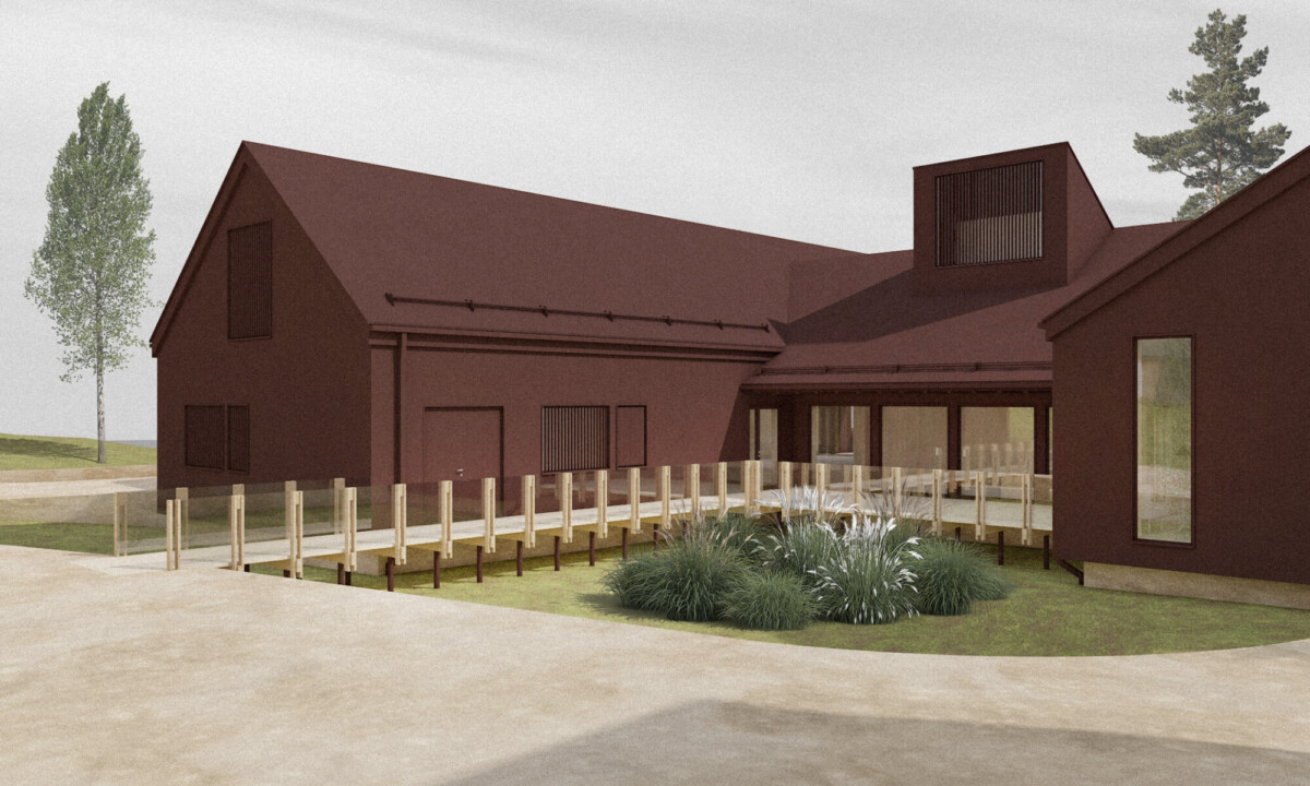 Moderni rakennus, jossa on tummanpunaiset ulkoseinät, suuret ikkunat ja puinen luiska sisäänkäynnille. Edessä on maisemoituja kasveja ja taustalla puita pilvisen taivaan alla.