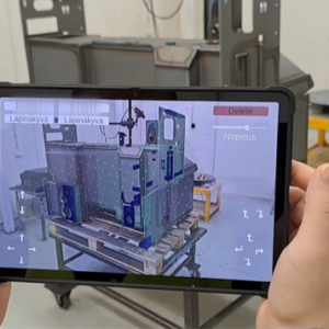 Henkilö pitää kädessään tablettia, joka näyttää metallirakenteen lisätyn todellisuuden päällekkäistä kuvaa, joka vastaa ja parantaa fyysistä esinettä työpöydällä teollisessa työpajaympäristössä.