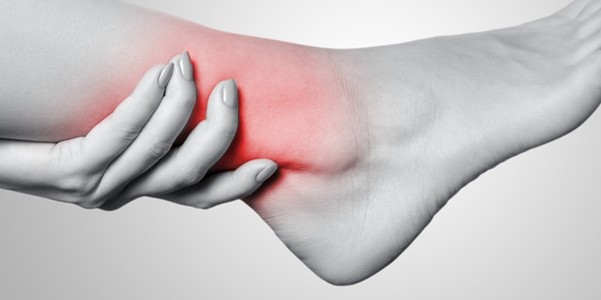Harmaasävykuva henkilöstä, joka pitelee nilkkaansa, jossa punainen alue korostaa kipua tai tulehdusta nilkkanivelen ympärillä.
