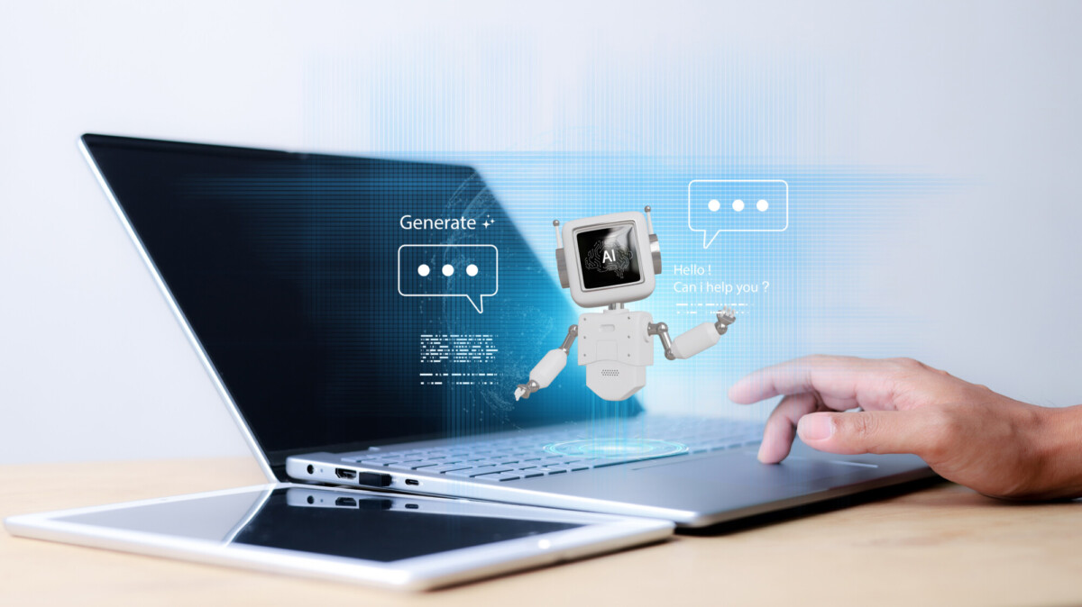 Henkilö kirjoittaa kannettavalla tietokoneella, jonka vieressä on tabletti. Näppäimistön yläpuolelle ilmestyy digitaalisesti pieni robotti, jolla on näyttö päässään ja joka näyttää keskustelukuplia ja tekstiä, jossa lukee: "Hei! Voinko auttaa?".