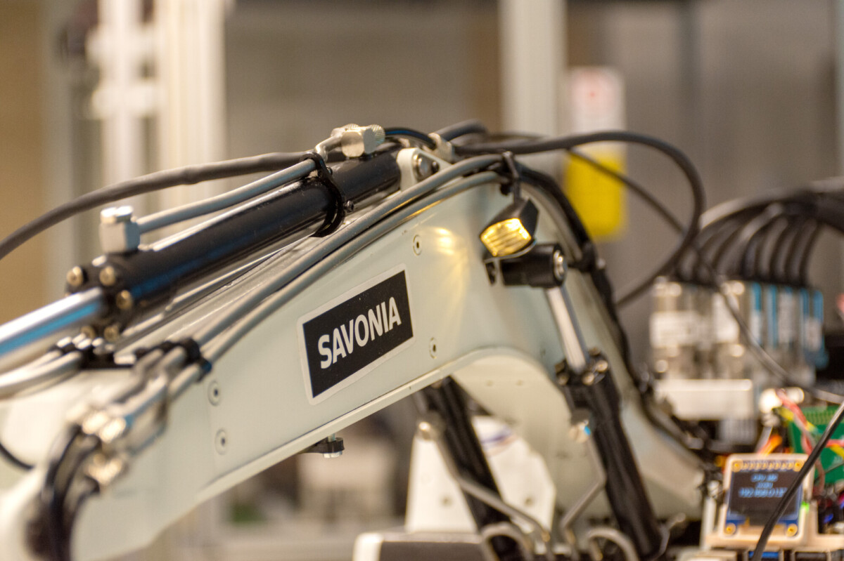 SAVONIA-merkityn robottikäsivarren lähikuva, jossa näkyy kaapeleita ja mekaanisia komponentteja laboratorio- tai teollisuusympäristössä.