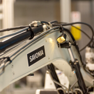 SAVONIA-merkityn robottikäsivarren lähikuva, jossa näkyy kaapeleita ja mekaanisia komponentteja laboratorio- tai teollisuusympäristössä.