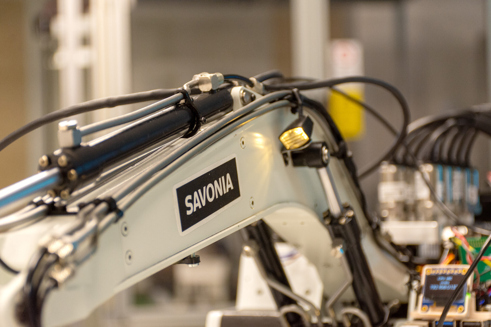 SAVONIA-merkityn robottikäsivarren lähikuva, jossa näkyy kaapeleita ja mekaanisia komponentteja laboratorio- tai teollisuusympäristössä.