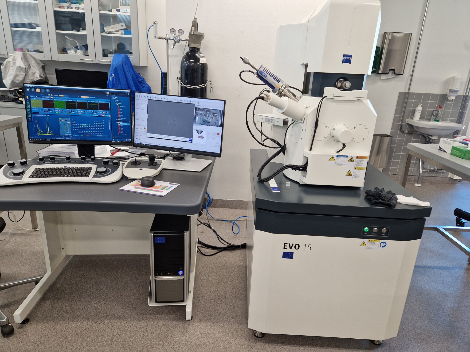 Laboratorio, jossa on EVO 15 -niminen pyyhkäisyelektronimikroskooppi, jonka vieressä on työpiste, jossa on kaksi näyttöä, joilla näytetään tieteellisiä tietoja, näppäimistö, tietokonehiiri ja ohjauspaneelit.