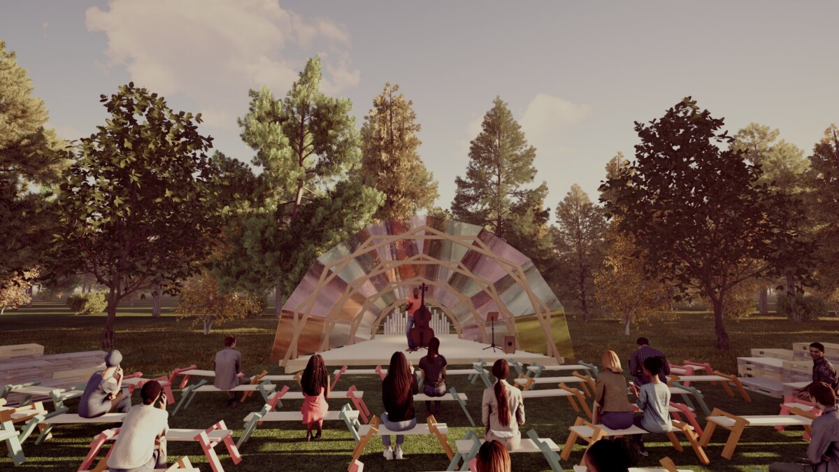 Ihmiset istuvat värikkäillä penkeillä ja katsovat esiintyjää pienellä ulkoilmalavalla, jossa on läpikuultava, kaareva katos. Näyttämö sijaitsee puiston puiden ympäröimänä osittain pilvisen taivaan alla.