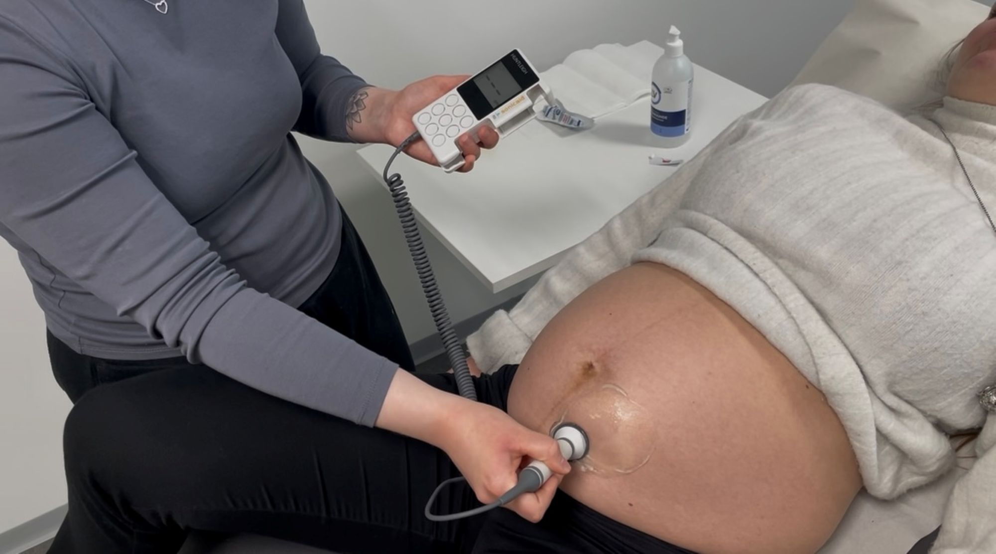 Henkilö käyttää kannettavaa Doppler-laitetta seuratakseen raskaana olevan naisen sydämenlyöntejä. Nainen makaa tutkimuspöydällä vatsa paljaana ja hänen iholleen on levitetty geeliä.