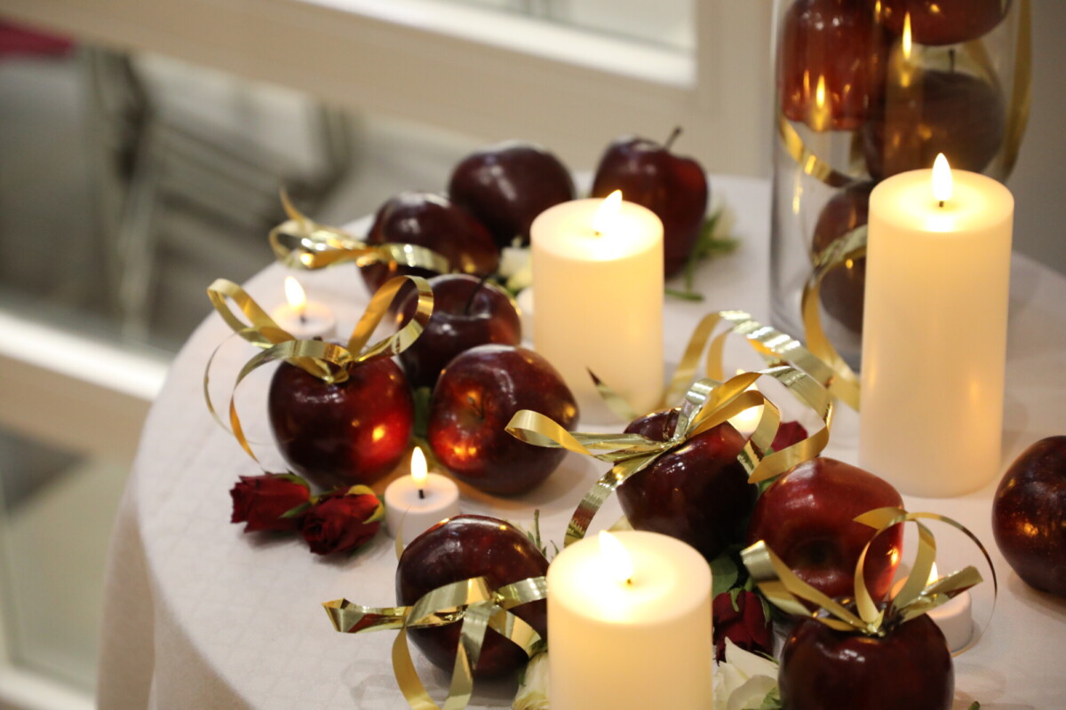 Pyöreä pöytä oli koristeltu punaisilla omenoilla, jotka oli sidottu kultanauhoilla, valkoisilla pylväskynttilöillä ja teekynttilöillä sekä muutamalla punaisella ruusulla, jotka loivat lämpimän ja juhlavan tunnelman.
