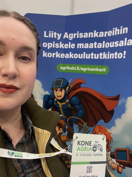 Nainen, jolla on virkamerkki, seisoo värikkään, piirroshahmoja esittävän banderollin edessä. Suomenkielinen teksti mainostaa maatalousalan opintoja ja tutkintoa, ja siinä on nettisivulinkki ja tapahtumatietoa KoneAgria 2025:stä Tampereella.