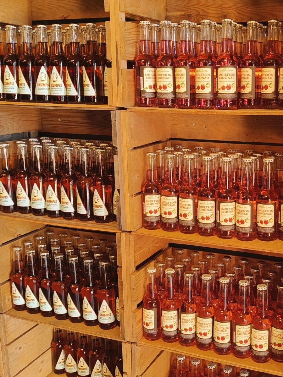 Puuhyllyt täynnä siististi aseteltuja punaisia ja kirkkaita juomapulloja, joissa kaikissa on kermanväriset etiketit.